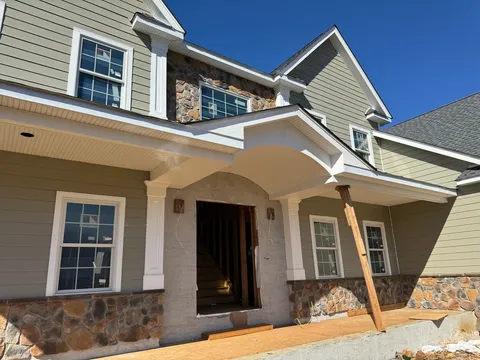 Sage lap home with a curved beadboard portico and fieldstone